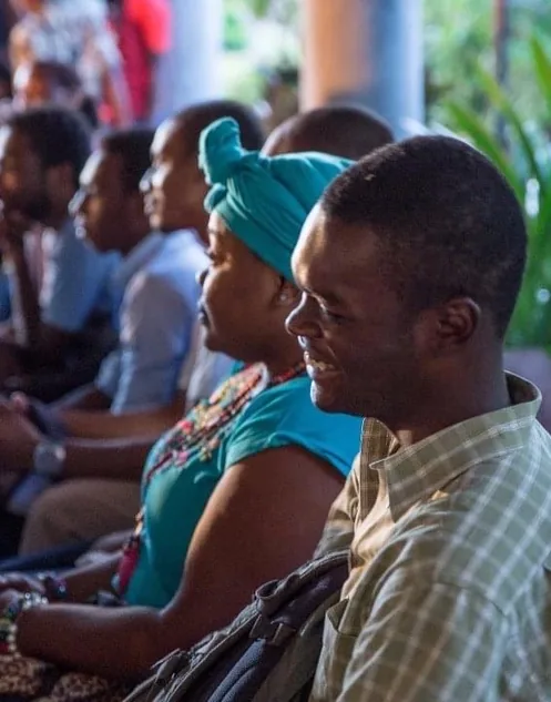 Audience members in profile, a woman in a turquoise head wrap smiling