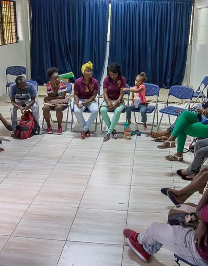 A discussion circle in a tiled room, people seated on blue chairs